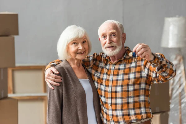 Hombre mayor abrazando esposa y sosteniendo llaves, concepto en movimiento - foto de stock