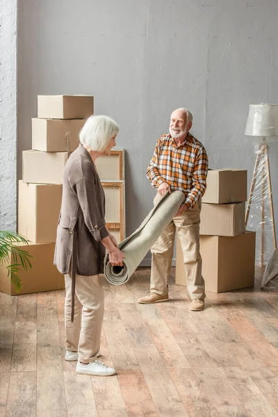 Full length view of senior couple rolling carpet in new house, moving concept — Stock Photo