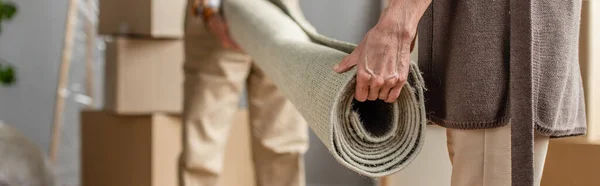 Panoramic shot of senior couple rolling carpet in new house, moving concept — Stock Photo