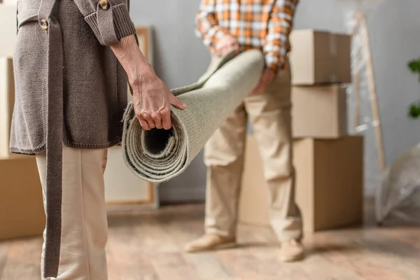 Cropped view of senior couple rolling carpet in new house, moving concept — Stock Photo