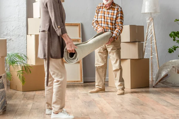 Cropped view of senior couple rolling carpet in new house, moving concept — Stock Photo