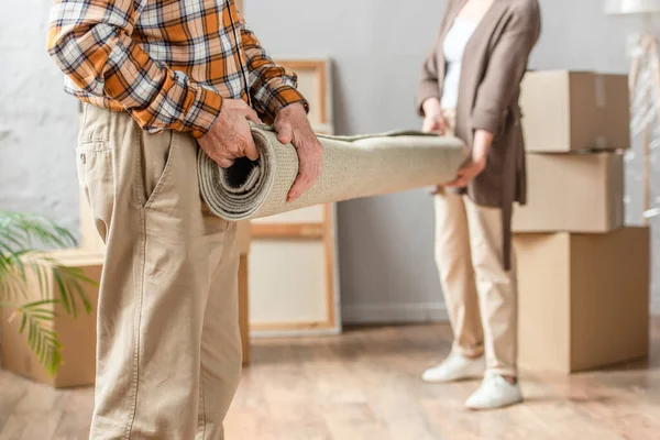 Cropped view of senior couple rolling carpet in new house, moving concept — Stock Photo