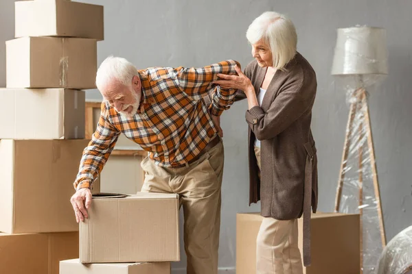 Senior leidet unter Rückenschmerzen und hält Kiste, während Frau Hilfe sucht — Stockfoto