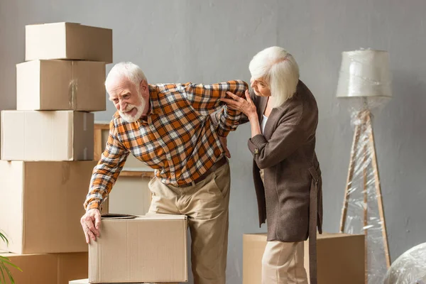 Senior leidet unter Rückenschmerzen und hält Kiste, während Frau Hilfe sucht — Stockfoto