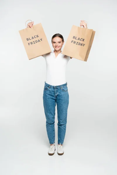 Young joyful woman holding shopping bags with black friday lettering on white — Stock Photo