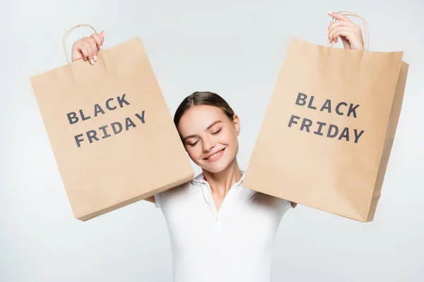 Jeune femme joyeuse avec les yeux fermés tenant des sacs à provisions avec lettrage noir vendredi isolé sur blanc — Photo de stock