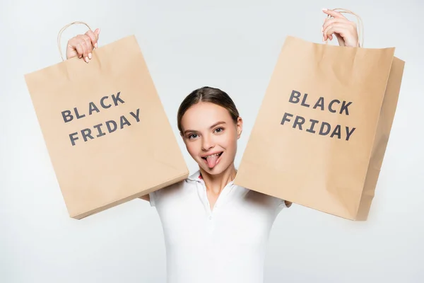 Jeune femme sortant la langue et tenant des sacs à provisions avec lettrage noir vendredi isolé sur blanc — Photo de stock
