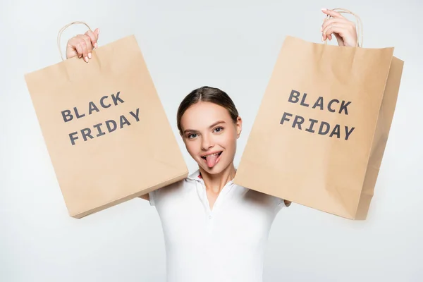 Young woman sticking out tongue and holding shopping bags with black friday lettering isolated on white — Stock Photo