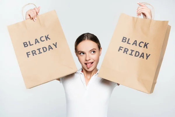 Jovem mulher saindo língua enquanto segurando sacos de compras com letras sexta-feira preto isolado no branco — Fotografia de Stock