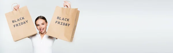 Panoramaaufnahme einer Frau, die die Zunge herausstreckt, während sie Einkaufstüten mit schwarzem Freitag-Schriftzug auf weißem Grund hält — Stockfoto