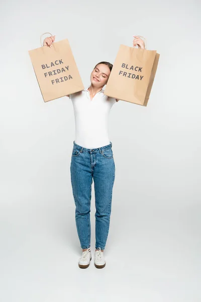 Jovem com olhos fechados segurando sacos de compras com letras sexta-feira preto no branco — Fotografia de Stock