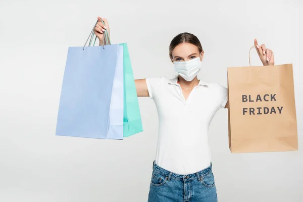 Jeune femme en masque médical tenant des sacs à provisions avec lettrage noir vendredi isolé sur blanc — Photo de stock