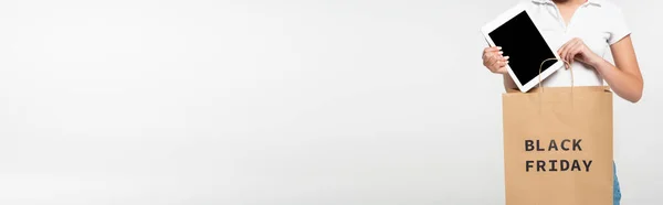 Vista ritagliata di donna mettendo tablet digitale con schermo bianco nella shopping bag con scritte nero venerdì isolato su bianco, scatto panoramico — Foto stock