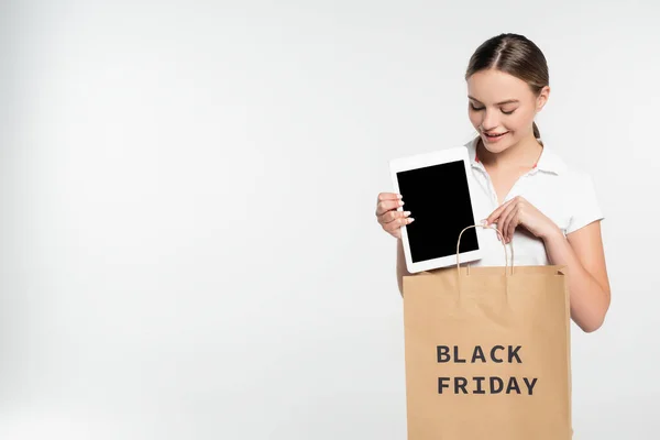 Jeune femme pointant du doigt la tablette numérique avec écran vierge près du sac à provisions avec lettrage noir vendredi isolé sur blanc — Photo de stock