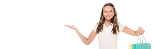 Concept panoramique de femme heureuse pointant avec la main et tenant des sacs à provisions isolés sur blanc — Photo de stock