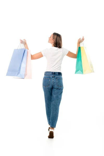 Vista posteriore di giovane donna in jeans che tiene borse della spesa isolate su bianco — Foto stock