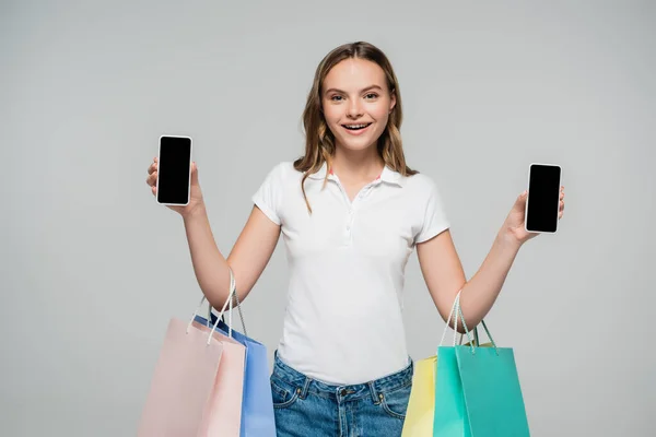 Joyeuse femme tenant smartphones avec écran vierge et sacs à provisions isolés sur gris, concept vendredi noir — Photo de stock