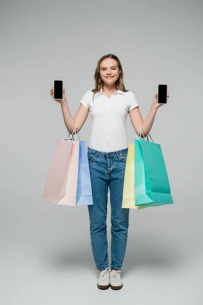 Giovane donna gioiosa in possesso di telefoni cellulari con schermo bianco e borse della spesa su grigio, concetto venerdì nero — Foto stock