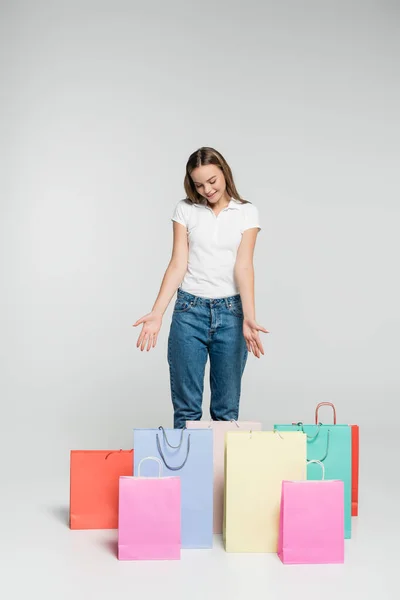 Joyeuse femme debout et pointant des mains vers les sacs à provisions sur gris, concept vendredi noir — Photo de stock