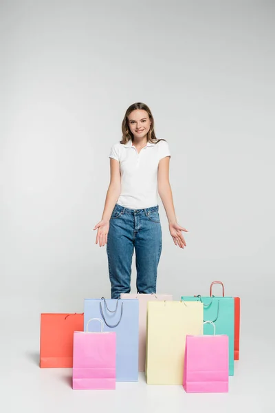 Joven mujer alegre de pie y señalando con las manos a las bolsas de compras en gris, concepto de viernes negro - foto de stock