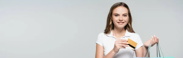 Horizontal image of joyful young woman holding credit card isolated on grey — Stock Photo