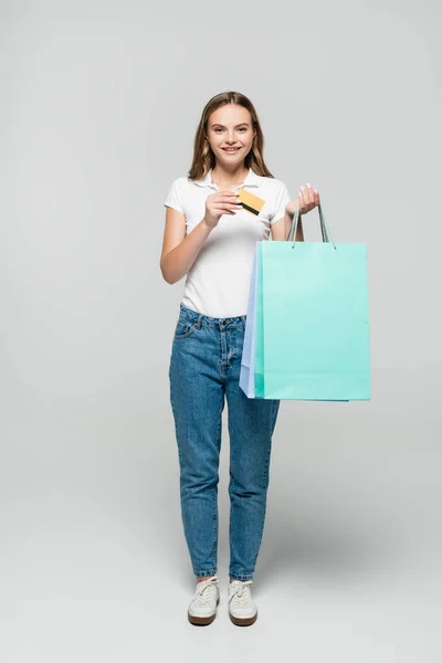 Gioiosa giovane donna in possesso di carta di credito e shopping bag blu su grigio, nero concetto venerdì — Foto stock