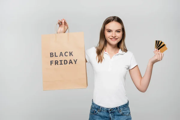 Задоволена жінка тримає кредитні картки та сумку з чорною п'ятничною пляшкою ізольовано на сірому — стокове фото