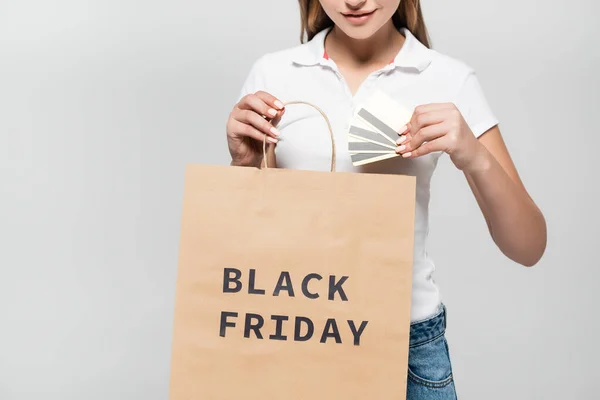 Обрізаний вид жінки, що тримає кредитні картки та сумку з чорною п'ятницею, написи ізольовані на сірому — стокове фото