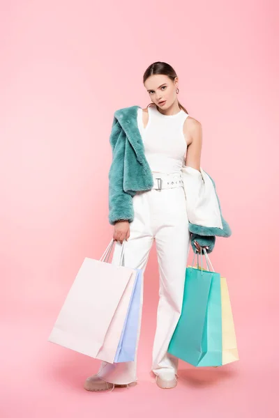 Mujer joven en chaqueta de piel sintética azul sosteniendo bolsas de compras en rosa, concepto de viernes negro - foto de stock