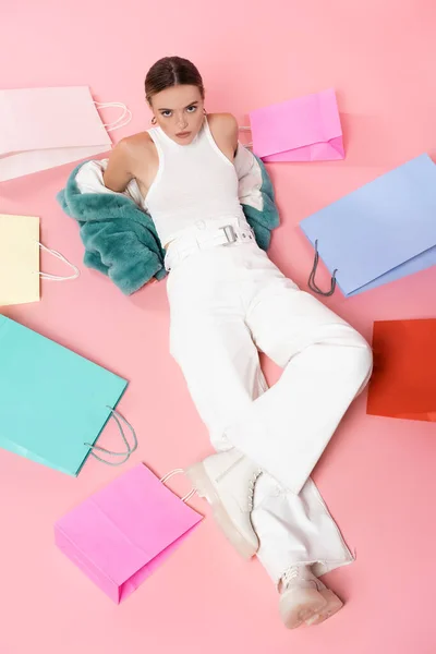 Vista aerea della giovane donna in giacca di eco-pelliccia blu seduta vicino alle borse della spesa sul concetto di venerdì rosa, nero — Foto stock