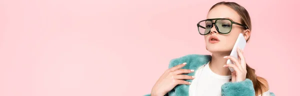 Plano panorámico de la mujer con estilo en gafas de sol hablando en el teléfono inteligente aislado en rosa - foto de stock