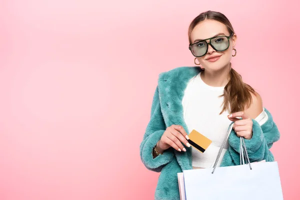 Mujer de moda en gafas de sol con tarjeta de crédito cerca de la bolsa de compras aislado en rosa, concepto de viernes negro - foto de stock