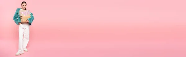 Concepto horizontal de mujer con estilo en gafas de sol que sostiene cajas con letras de zapatos favoritos en rosa, concepto de viernes negro - foto de stock