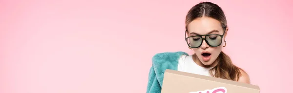 Shocked woman in sunglasses holding box isolated on pink, black friday concept — Stock Photo