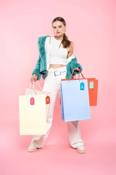 Elegante cliente joven sosteniendo bolsas de compras con etiquetas de venta en rosa, concepto de viernes negro - foto de stock