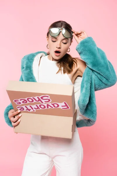Surprised woman in sunglasses looking at box with favorite shoes lettering on pink, black friday concept — Stock Photo