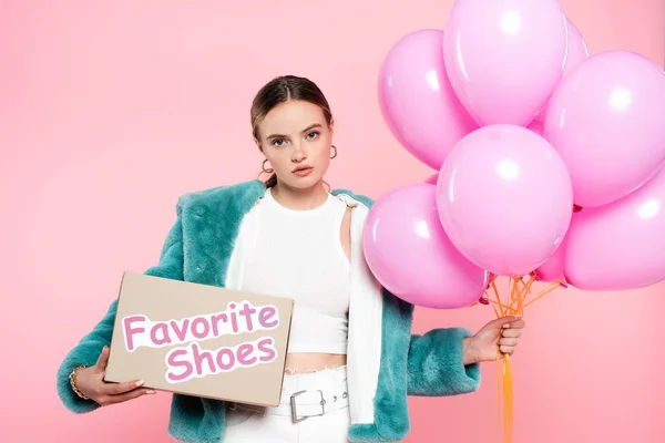 Junge Frau hält Karton mit Lieblingsschuhen Schriftzug und Luftballons auf rosa — Stockfoto