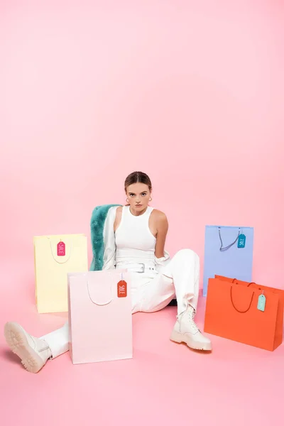 Giovane cliente seduto vicino a borse della spesa con tag di vendita sul rosa, concetto di venerdì nero — Foto stock