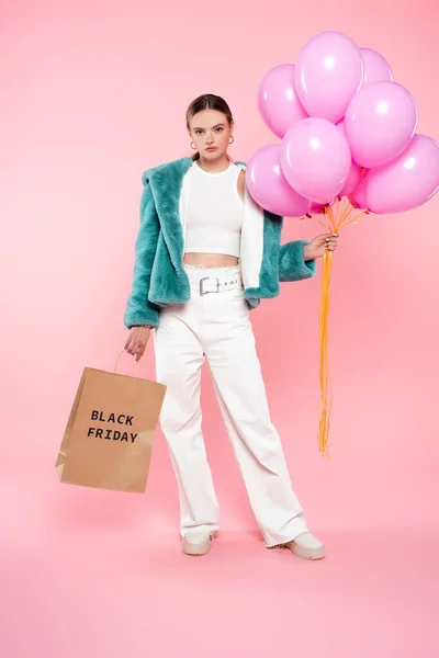 Jeune femme tenant sac à provisions avec lettrage noir vendredi et ballons sur rose — Photo de stock