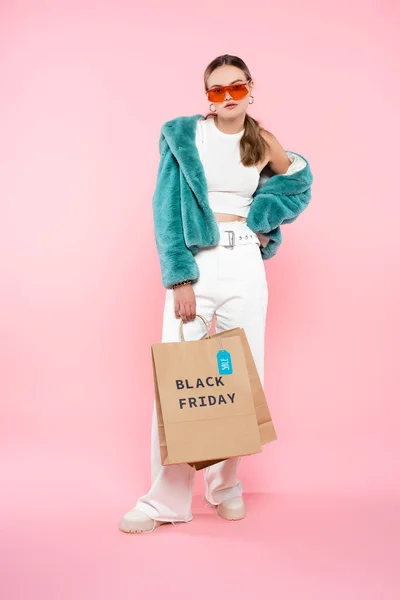 Young woman holding shopping bag with black friday lettering and sale tag on pink — Stock Photo