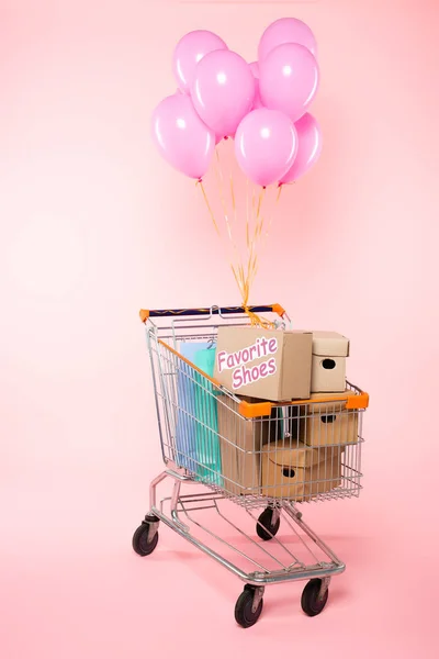 Тележка с пакетами для покупок и коробками возле воздушных шаров на розовой, черной пятничной концепции — стоковое фото