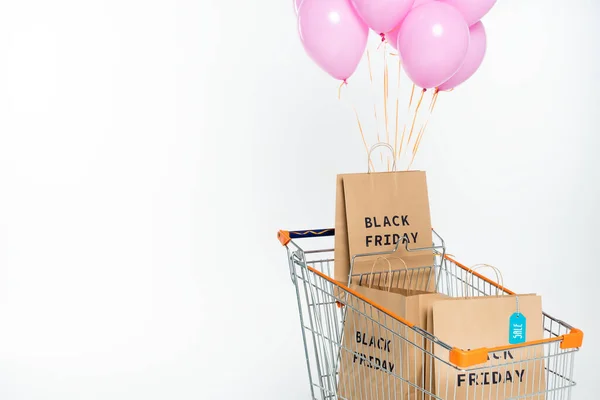 Shopping bags with black friday lettering in trolley with pink balloons on white — Stock Photo