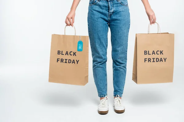 Cropped view of customer holding shopping bags with sale tag and black friday lettering on white — Stock Photo