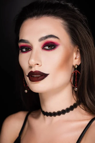 Young woman with dark makeup and accessories looking at camera isolated on black — Stock Photo