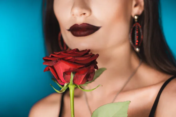 Vista recortada de la mujer con lápiz labial negro cerca de rosa roja en azul - foto de stock