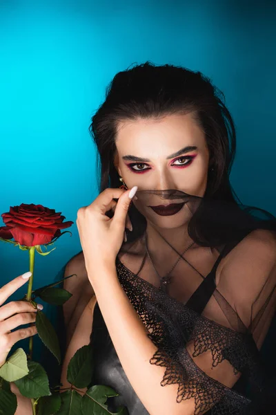 Evil bride with dark makeup holding rose and veil on blue — Stock Photo