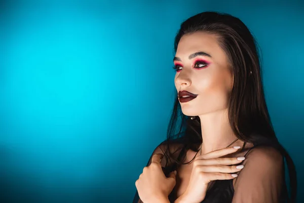 Geheimnisvolle junge Frau mit dunklem Make-up schaut weg auf blau — Stockfoto