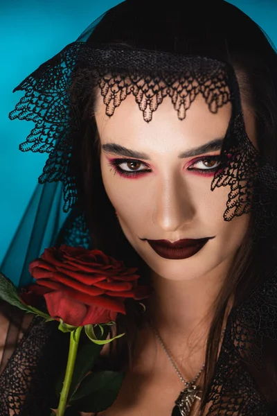 Jeune femme avec maquillage noir en voile foncé près de rose sur bleu — Photo de stock