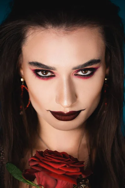Mystérieuse jeune femme avec maquillage noir regardant la caméra près de rose — Photo de stock