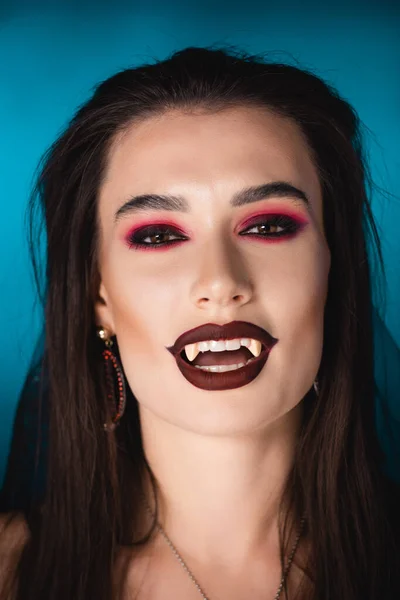 Брюнетка вампир с черным макияжем и белыми страшными зубами на голубом — стоковое фото
